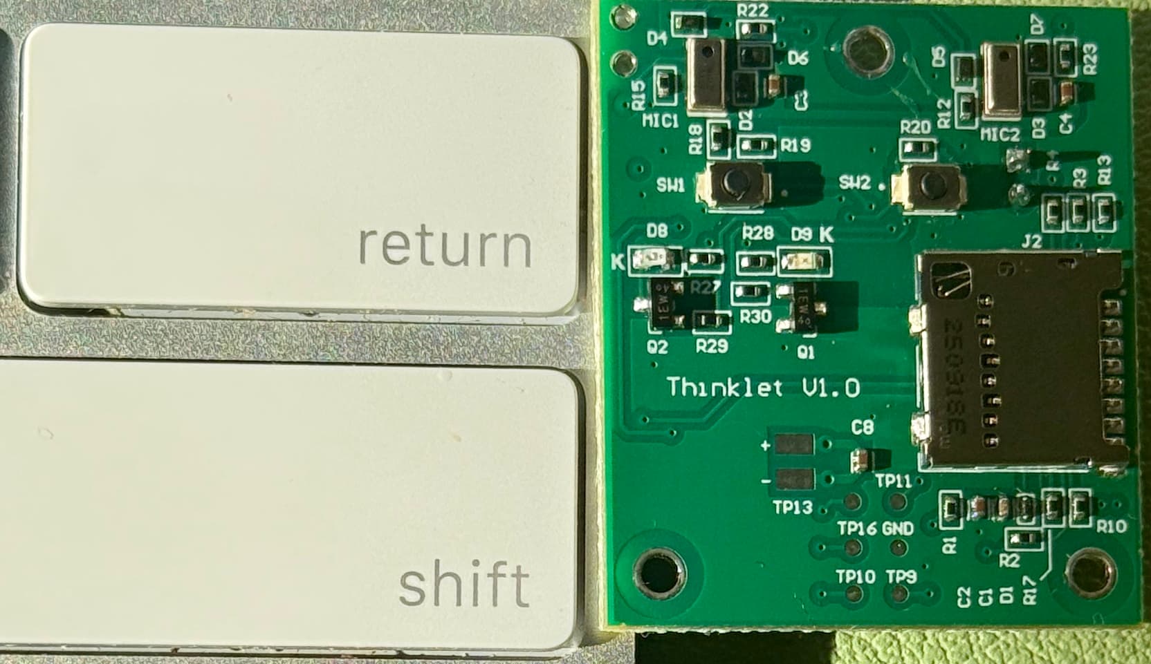 Thinklet V1.0 green PCB with microphones, buttons, and microSD slot, shown next to keyboard keys for scale